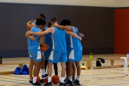 Diverse male basketball players embracing and holding basketball at gym. Sport, activity, togetherness and lifestyle, unaltered.